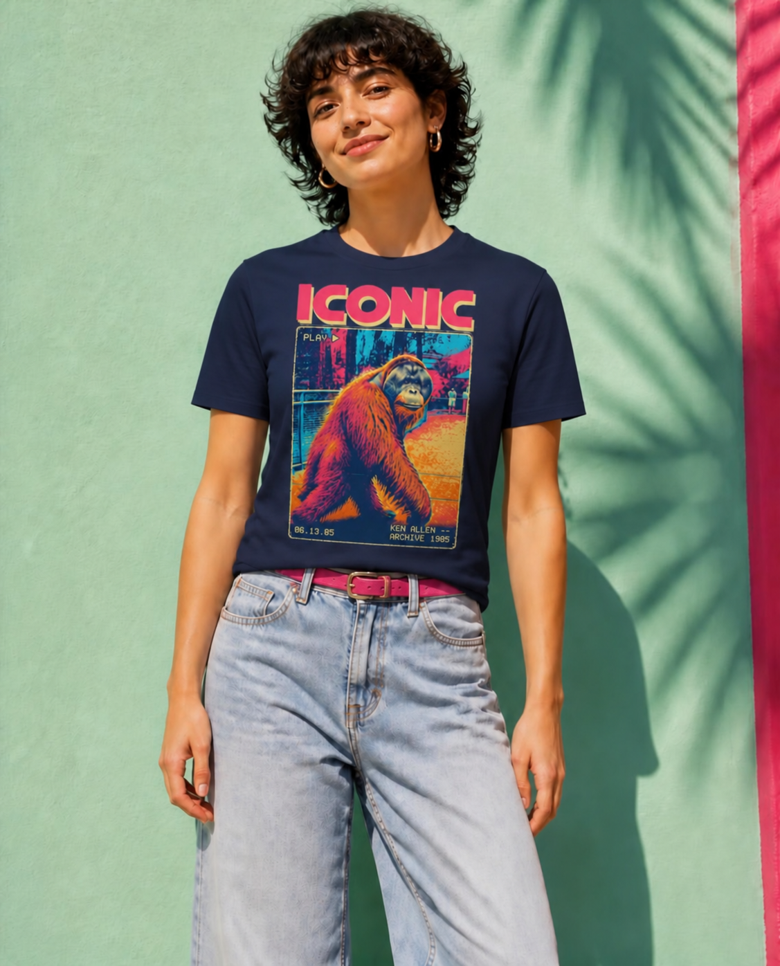 Front view of the Navy Ken Allen Iconic graphic tee with flat short sleeves and colorful VHS artwork against a mint and pink wall