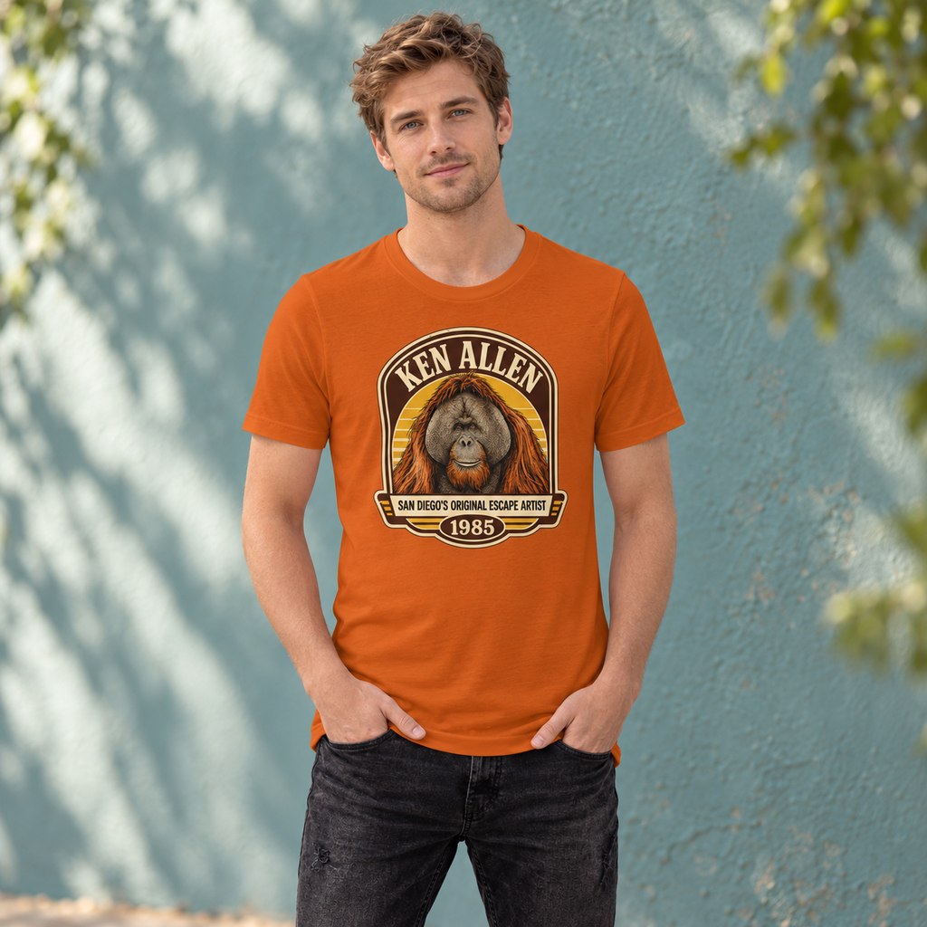 Autumn Ken Allen Heritage tee with retro orangutan badge artwork against a teal courtyard wall
